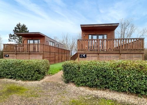 a wooden house with a balcony and bushes at Fenview Lakes in Ely