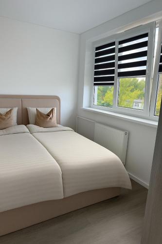 een witte slaapkamer met een bed en twee ramen bij Feliz Stay in Šiauliai
