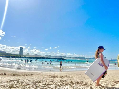 una donna in piedi sulla spiaggia con una tavola da surf di 2 BR Burleigh Beach Family Apartment a Gold Coast