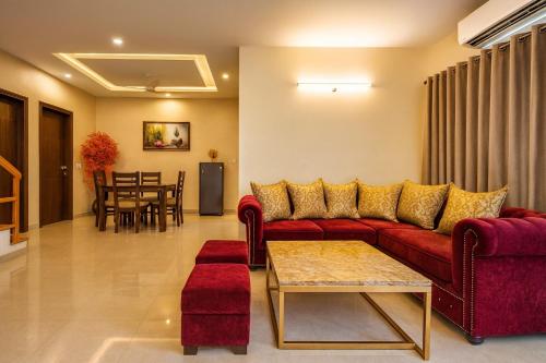a living room with a red couch and a table at Pearl Grand Boutique Cottage in Omaxe Anandam Vrindavan - #premium AC rooms with balcony #big parking #lift #garden #peaceful area #near prem mandir #property of the year #most awarded in Vrindāvan