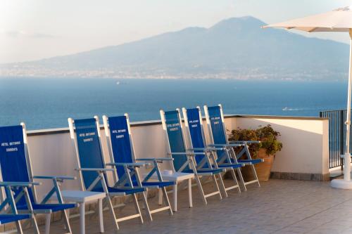 a row of blue chairs on a balcony overlooking the water at Hotel Britannia in Sorrento