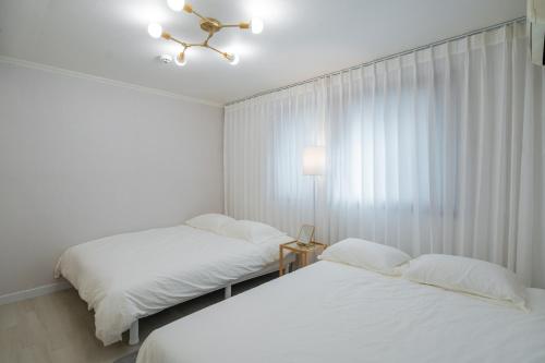 two beds in a white room with a window at Cozy Haven in Suwŏn-yŏk