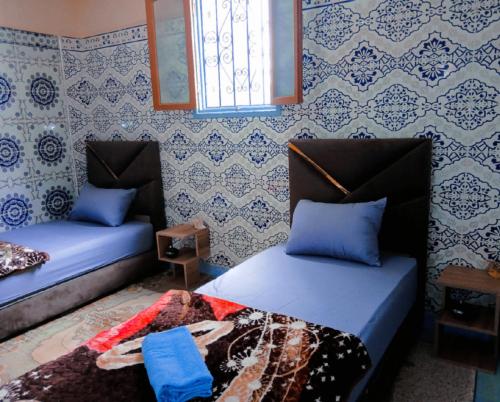 two beds in a room with blue and white wallpaper at Tayrt Hostel in Mirleft