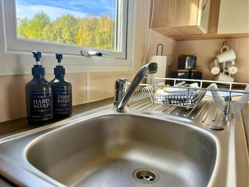 a kitchen sink with two bottles of soap and a window at Lovely Hot Tub Caravan in Northumberland, Free Golf Access, Dog Friendly in Swarland
