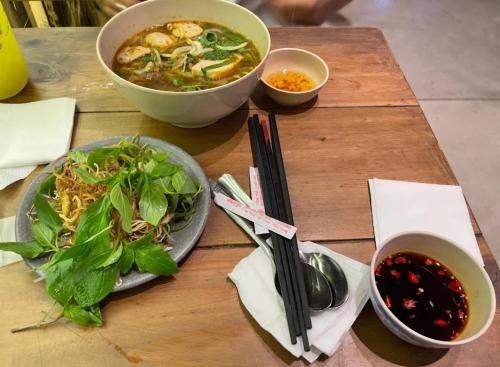 ホーチミン・シティにあるBinh Minh Homstayのスープとサラダが入った2つのボウルが置かれた木製のテーブル