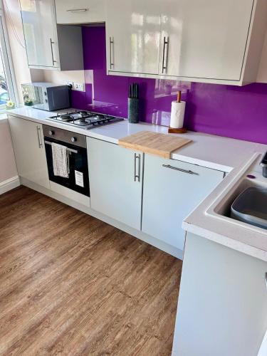 a kitchen with white cabinets and purple walls at Denzels Den Apartment 2 in Llandudno Junction