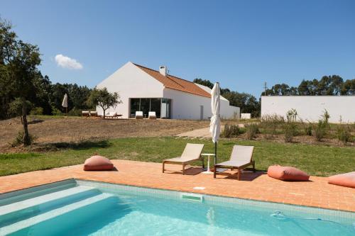 a swimming pool with two chairs and an umbrella at Casa do Regadio in Zambujeira do Mar