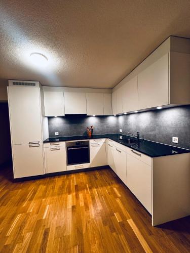 a kitchen with white cabinets and a wooden floor at Modernes City Apartment am See, Zentral in Rorschach
