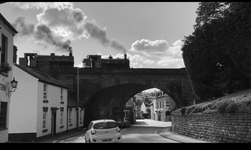 a train crossing a bridge over a street with a car at Whispering Place Georgian Grade II Sleeps 6 Adults 3 mins from Safari Park & Steam Train in Bewdley