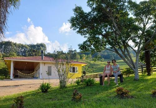 two women sitting in front of a yellow house at Sítio Vô Quirino in Barracão