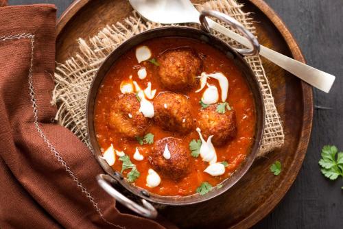 a bowl of meatballs in a stew on a wooden plate at Capital O De Alphabet Kakinada in Kākināda