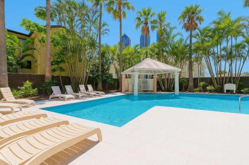 a swimming pool with chairs and a gazebo and palm trees at Hotel Room Ocean View Surfers Paradise in Gold Coast