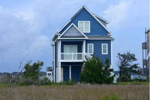 a blue house with a balcony on a field at Harkers Hideaway - Waterfront with Private Beach in Harkers Island