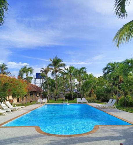a large swimming pool with chairs and palm trees at The Golddiggers Resort in Nai Yang Beach