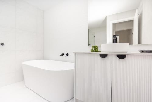 Un baño blanco con bañera y lavabo. en Luxury Hope Island Retreat, en Gold Coast