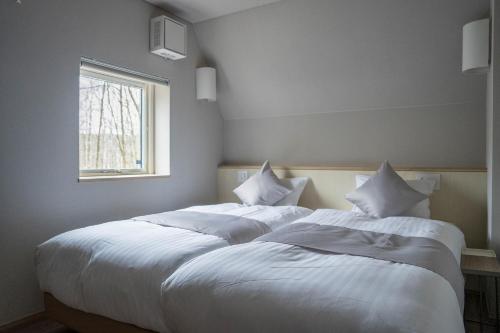 a bedroom with two beds with white sheets and a window at ERUSA Rusutsu in Rusutsu