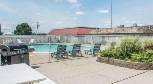 a pool with chairs and a grill next to a fence at Quality Inn in Geneseo