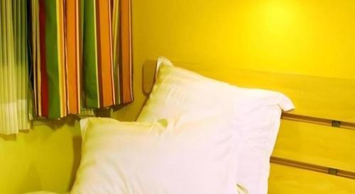 a bed with a white pillow against a yellow wall at 7 Days Inn Luoyang Railway Station Wangcheng Avenue in Luoyang