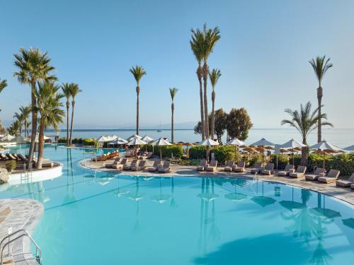 a large swimming pool with chairs and palm trees at Grecotel LUXME Kos in Kos Town