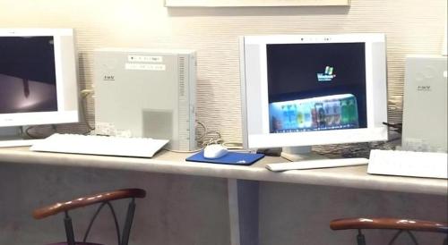 three computer monitors sitting on a desk with two chairs at Alpha Hotel Tokushima in Tokushima