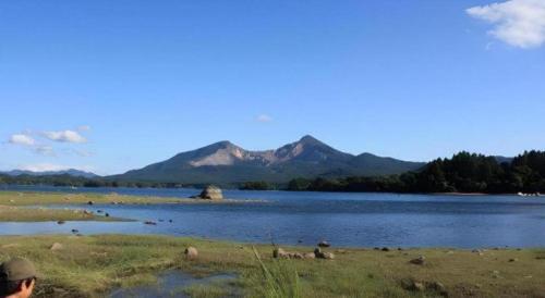 a man standing next to a body of water with mountains at Petit Hotel Hoshi no Shizuku in Kitashiobara