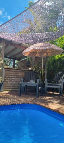 a patio with two chairs and an umbrella and a pool at Zananas Bungalow privé chez l'habitant in Saint-Paul