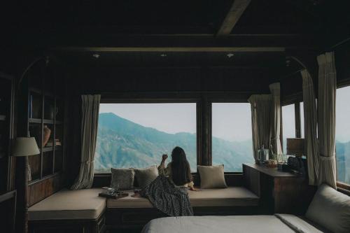 a woman sitting on a bed looking out of a window at MiAmi Mountain Retreat in Bắc Yên