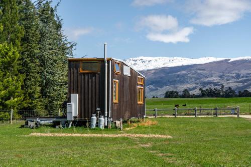 une petite maison dans un champ avec des montagnes en arrière-plan dans l'établissement Tarras Tiny Haven - Wake up to Breathtaking Mountains, à Tarras