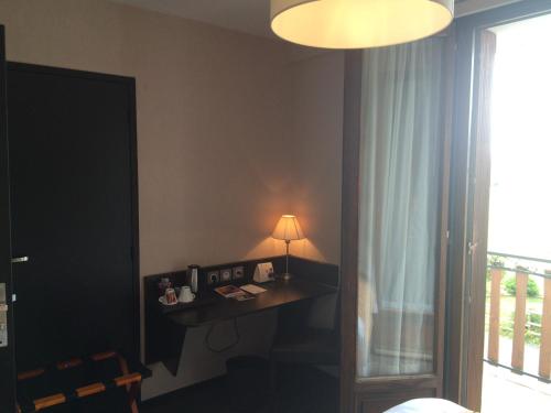 um quarto com uma secretária com um candeeiro e uma janela em Auberge de la Petite Ferme, Super-Besse Est, The Originals Relais (Qualys-Hotel) em Besse-et-Saint-Anastaise