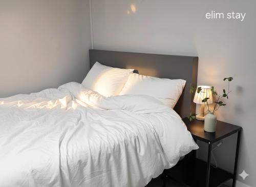 アンサンにあるElimhouseのベッド(白いシーツ付)、サイドテーブル(ランプ付)
