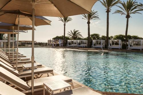 a pool with chairs and umbrellas and palm trees at The Site Hotel Ibiza New Opening 2026 in Playa d'en Bossa
