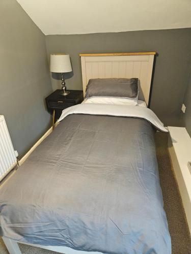 Una cama grande en un dormitorio con una mesita de noche y una lámpara. en The coach house, en Nottingham