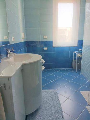 a blue tiled bathroom with a sink and a toilet at Appartamento Guido in Monfalcone
