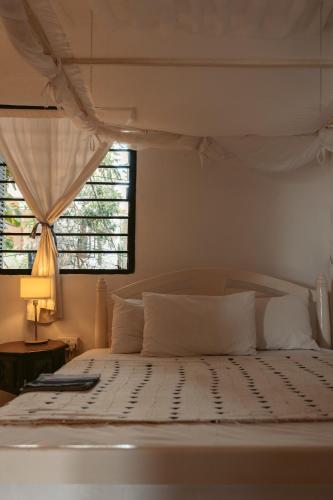 a bedroom with a white bed with a window at Banana House and Wellness Centre in Lamu