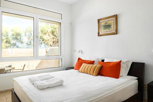 a white bed with orange pillows and a window at Hatsuk 18 in Bet Yannay