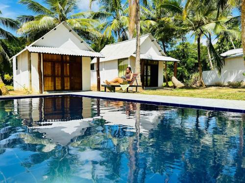 a woman sitting in a chair next to a house with a swimming pool at River Side & Swimming pool in Udawalawe
