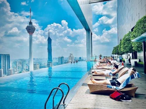 a pool on the roof of a building with people laying on chairs at Platinum KLCC by Like Home KUALA LUMPUR in Kuala Lumpur