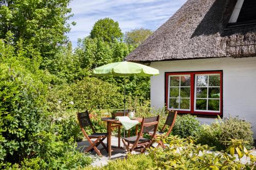 a table and chairs with an umbrella in front of a house at Reetdachhaus mit Nähe zur Ostsee, Außensauna, Spielplatz & großem Garten in Manhagen