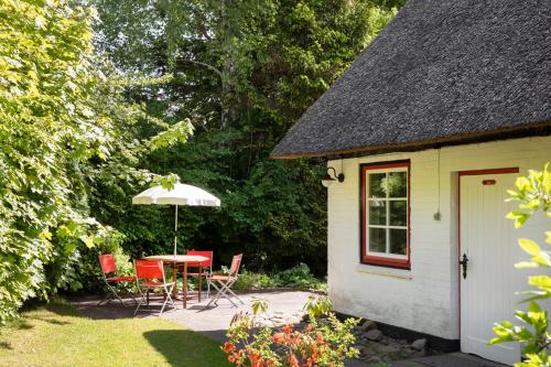 a table and chairs with an umbrella next to a shed at Reetdachhaus mit Nähe zur Ostsee, Außensauna, Spielplatz & großem Garten in Manhagen