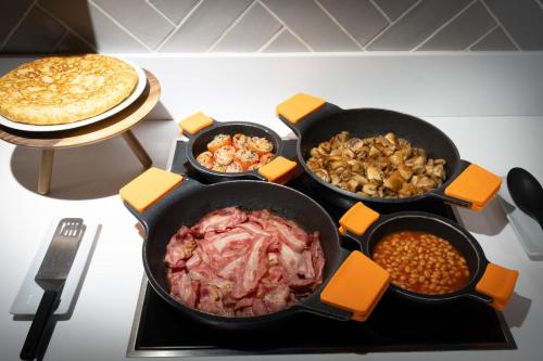 a table with four pans of food and a pie at voco Bilbao - City by IHG in Bilbao
