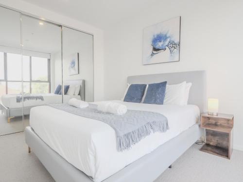 a white bedroom with a large bed and a mirror at Stylish 1BR1BA apt in Footscray Pool Gym WIFI in Melbourne