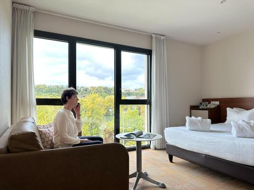 a man sitting on a couch in a hotel room with a window at Hôtel Lyon Métropole in Lyon