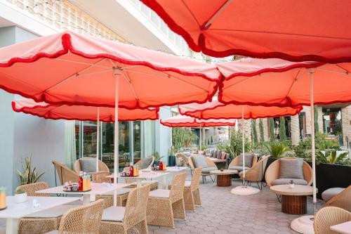 a row of tables with red umbrellas on a patio at Kimpton Rowan Palm Springs Hotel by IHG in Palm Springs