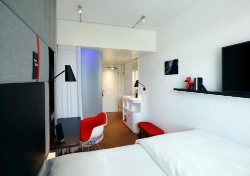 a bedroom with two white beds and a red chair at citizenM Zürich in Zürich