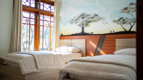 two beds in a room with a painting on the wall at Ijen Vibe's Inn in Banyuwangi