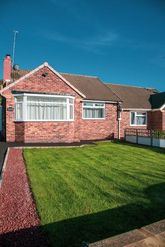 a brick house with a green lawn in front of it at Villa Emma - Modern Bungalow with EV Point, Free Parking & Workspace in Northampton