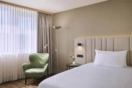 a hotel room with a bed and a green chair at NH Leipzig Messe in Leipzig