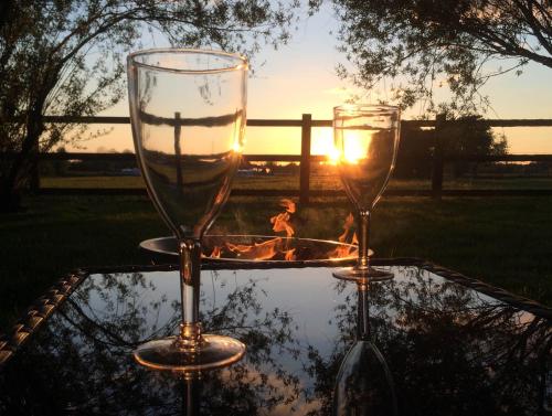 two wine glasses sitting on a table with the sunset in the background at Oxford Riverside Glamping in Oxford