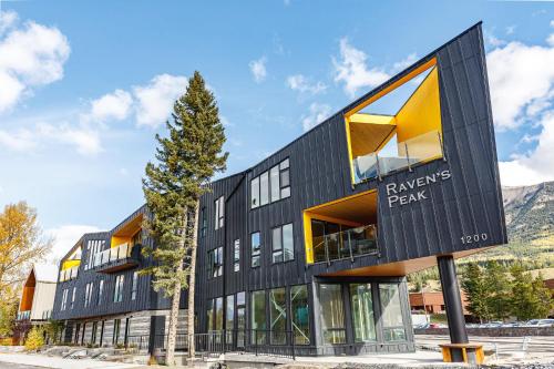 a black building with yellow windows and a tree at Ravens Nest - Private Hot Tub in Canmore