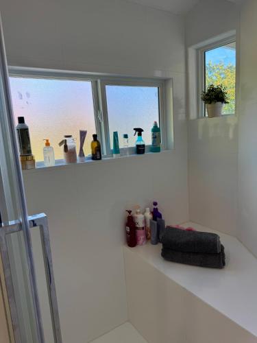 a white bathroom with two windows and bottles on a shelf at Maple & Moon in Richmond